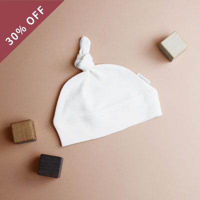 A flatlay of a Organic Top-Knot Hat in White. 30% OFF.