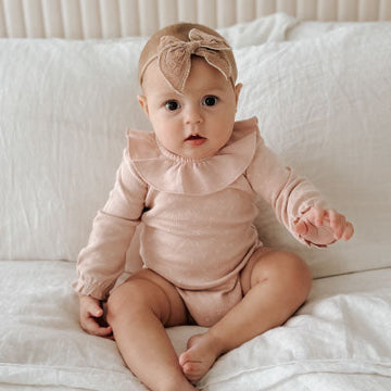 An infant girl wearing a pink outfit.