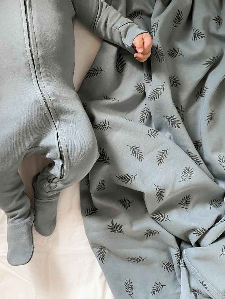 Child wearing Organic Swaddling Blanket, Print in Pool Fern.